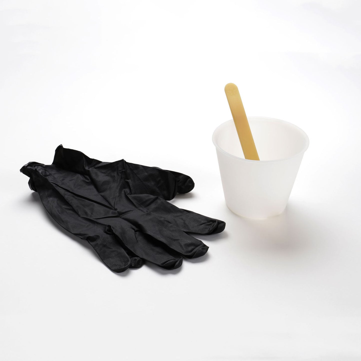 Photo: A large pair of black nitrile (disposable) gloves next to a translucent-clear silicone mixing cup with a beeswax-colored polyurethane mixing stick.