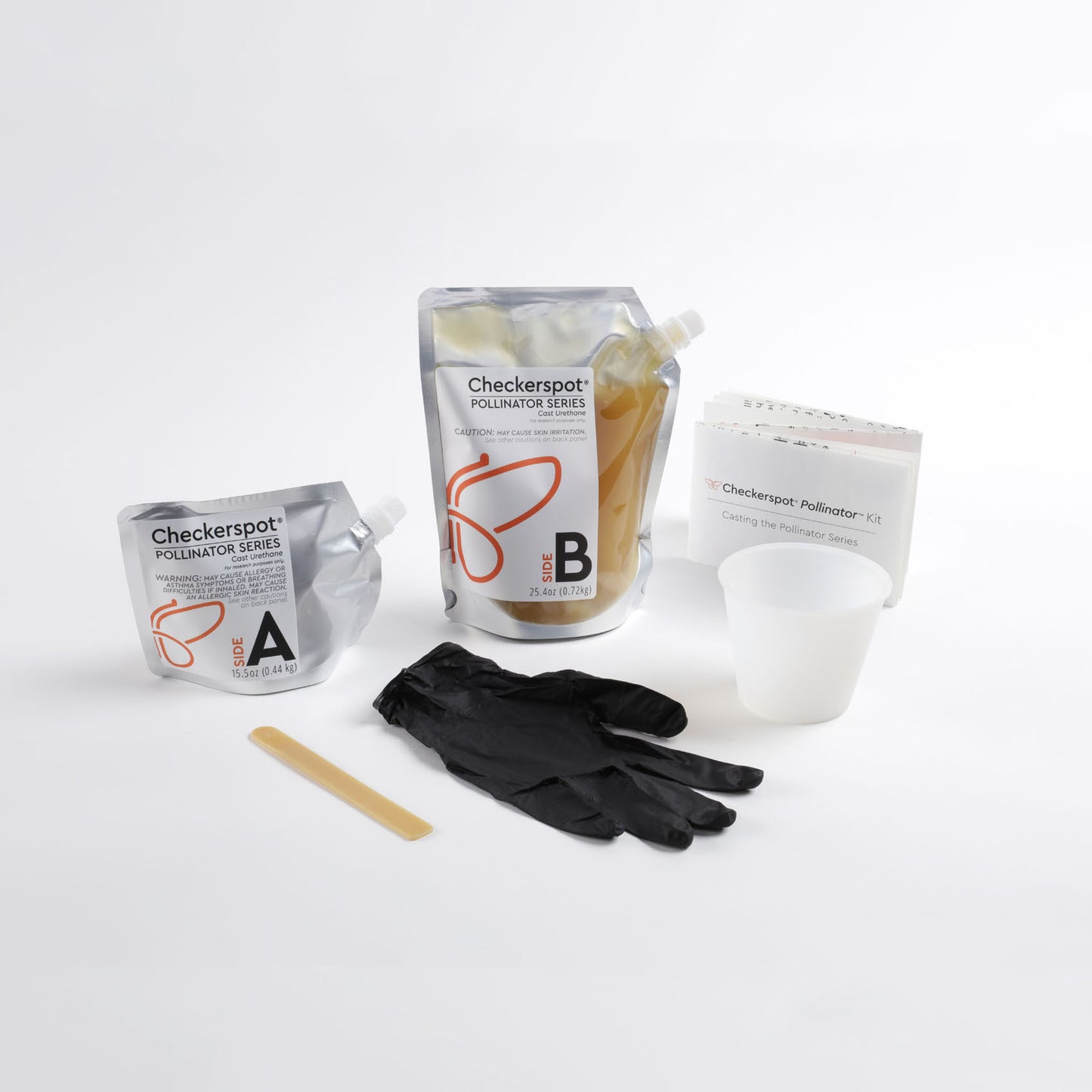 Photo: 6 objects on a white background. In the back row, there is a small aluminum spouted pouch that says "Side A" on it. Next to it is a clear and aluminum flexible spouted pouch that says "Side B", with a beeswax-colored liquid material inside. To the right is a white folded piece of paper that says “Checkerspot® Pollinator™ Kit, Casting the Pollinator Series”. In the front row is a translucent silicone cup, a large pair of disposable black gloves, and a beeswax colored polyurethane mixing stick. 